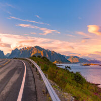 Panorama of empty winding country road in Norway, Europe, Scandinavia. Auto travel on sunset. Blue sky with clouds and mountains. Lofoten islands.