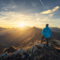 Man on stone on the hill and beautiful mountains in haze at colorful sunset in autumn. Dolomites, Italy. Sporty guy, mountain ridges in fog, orange grass and trees, blue sky with sun in fall. Hiking
1443409611