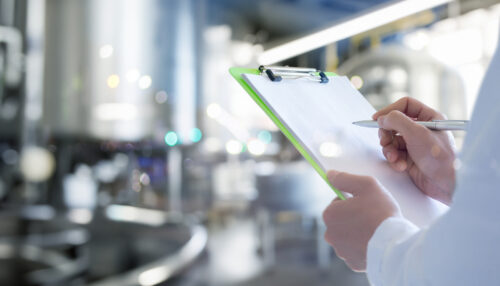 An engineer in a production facility makes entries in a journal.